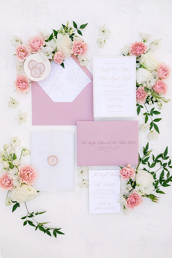 Wedding invitation suite with blush wedding invitations, pink envelope, calligraphy cards, wax seals, and roses on a white textured surface
