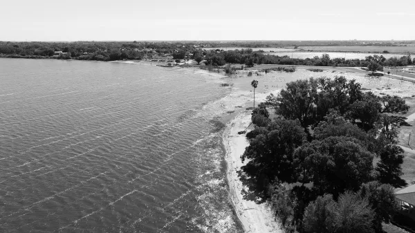 Lakeside landscape with aerial lake view showing a curving shoreline, tree-lined edge, road and bridge over water beneath open sky