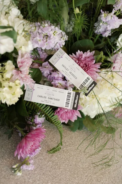 Wedding place cards arranged as an escort cards idea among flowers and fern greenery on a stone floor, like ticket-style seating assignments