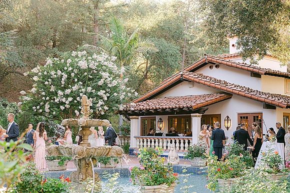 Wedding cocktail hour with outdoor wedding cocktails around cocktail tables near a stone fountain in a Spanish-style villa courtyard under string lights