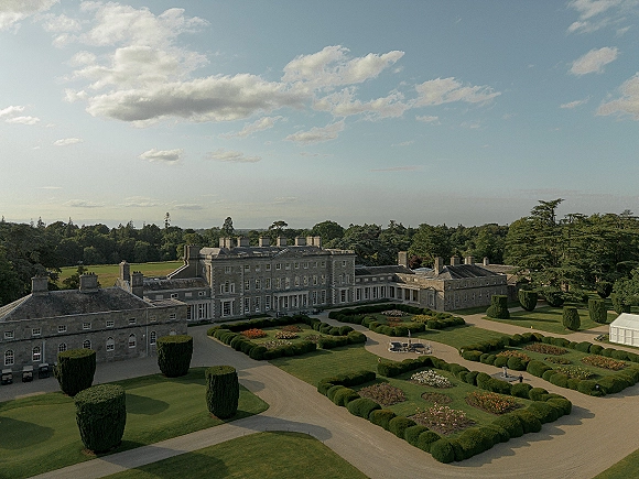Wedding venue exterior with an estate wedding venue stone manor house, manicured hedges and formal beds around a fountain by a gravel drive