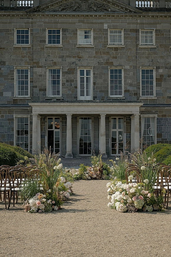 Ceremony aisle decor with floral aisle arrangements of pastel roses, hydrangeas and greenery along a gravel runner in a stone manor courtyard