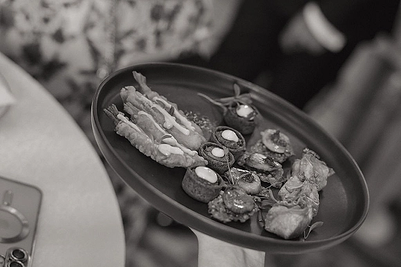 Wedding cocktail appetizers on a serving tray with assorted bite-size canapés, dipping sauce, and microgreens as guest hands reach in at reception