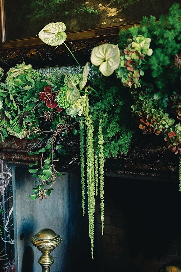 Wedding floral installation with greenery mantle decor cascading over a fireplace mantel, framed by an ornate mirror against dark walls