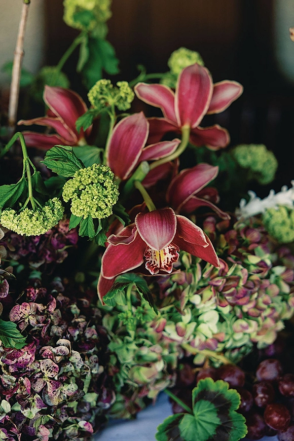 Wedding floral arrangement with burgundy orchid centerpiece, hydrangea blooms and green viburnum, lush greenery against a dark backdrop