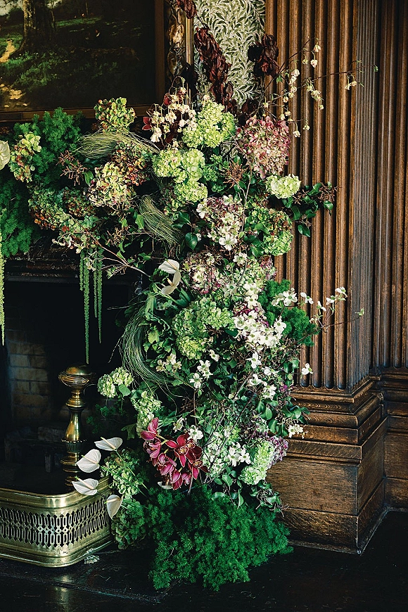 Wedding floral installation with a fireplace floral arrangement of hydrangeas, orchids, anthurium, and greenery on a wood-paneled hearth