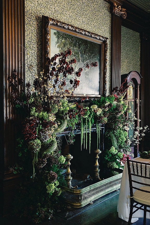 Fireplace floral installation with mantel greenery garland, cascading hydrangea and amaranthus over a vintage mantel in a moody paneled room