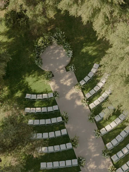 Ceremony setup with outdoor ceremony seating in a semicircle around a circular ceremony platform on a garden lawn bordered by trees.