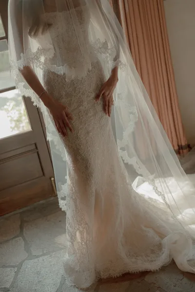 Wedding dress close-up of a lace bridal gown with delicate lace appliqué and scalloped hem, fitted through the bodice and flaring at the skirt