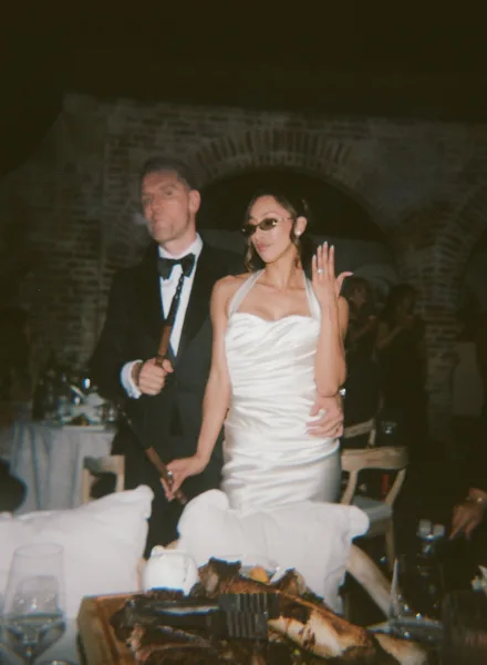 Couple portrait with the bride showing her ring pose beside the groom, smiling beneath a brick archway during the reception.