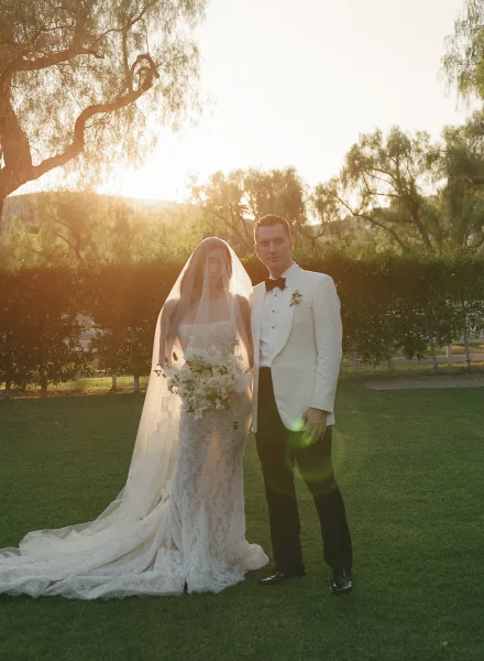 Couple portrait of a bride and groom standing in a garden at golden hour, her cathedral veil flowing as sunset paints the hills.
