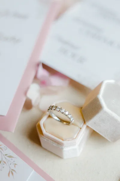 Wedding ring diamond wedding band in a white velvet hexagon box on pink invitation cards with ribbon, styled on a soft neutral surface