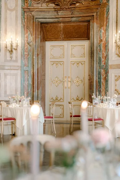 Reception tablescape with round wedding reception tables, white linens, taper candles, and floral centerpieces in a marble-walled banquet hall