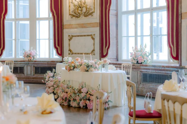 Reception tablescape with round wedding tables, white tablecloths, pastel florals and taper candles beneath tall windows and red drapes