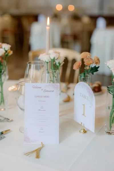 Reception tablescape with wedding menu card, peach and white bud vases, and a taper candle in softly lit reception room