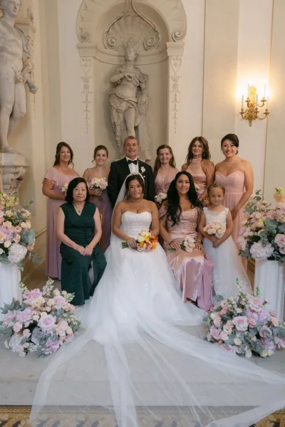 Wedding party portrait with bride in strapless ball gown and veil holding a bouquet, posed with bridesmaids in ornate marble hall