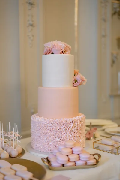 Wedding cake three tier wedding cake with blush ruffle buttercream and rose sugar flowers on a dessert table in an indoor reception room