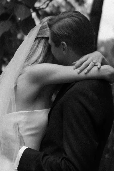 First dance as bride and groom dancing in a close embrace, bridal veil trailing, wedding guests watching in an indoor reception space