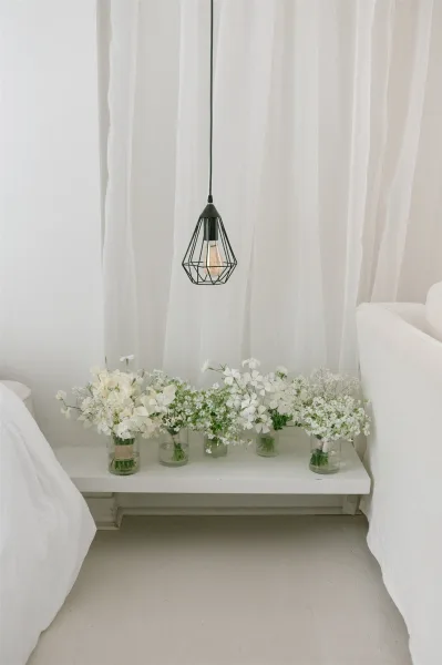 Wedding bouquet display of white bridal bouquets in bud vases and glass jars on a table beneath a pendant light in a bright suite