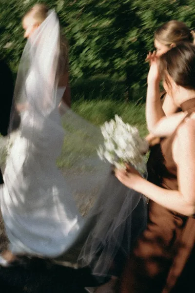 Wedding exit moment as bride walks away under a long bridal veil while bridesmaids cheer with white bouquets on a garden path
