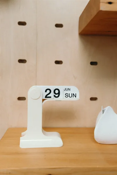 Wedding date detail on a flip desk calendar atop a wooden surface beside a white ceramic decor object on a minimalist shelf