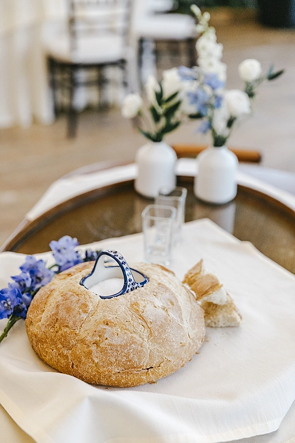 Wedding bread bowl with salt set on a rustic loaf, blue-patterned ceramic bowl and blue and white florals on a wooden tray indoors