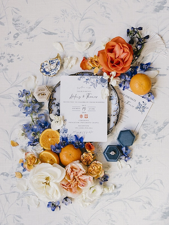 Invitation suite wedding invitation flat lay with save the date, rings in boxes, rose petals, blue flowers and oranges on patterned linen