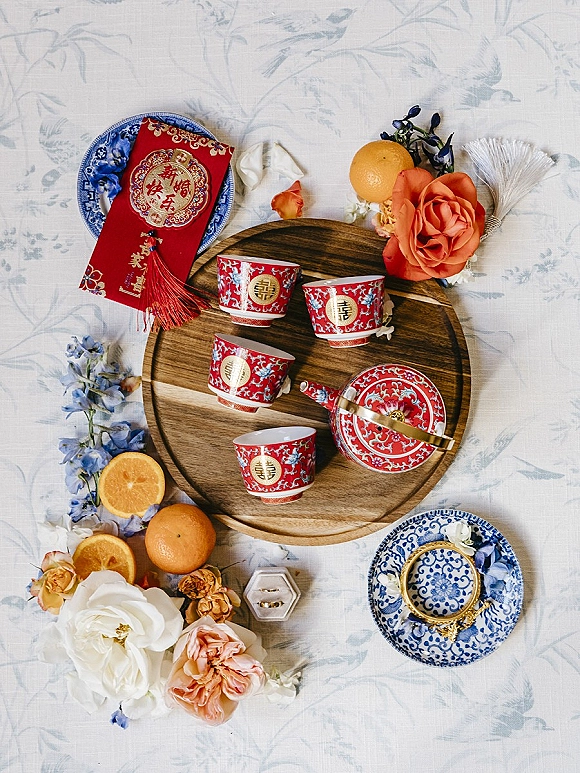 Tea ceremony details with Chinese tea ceremony setup, red cups, rings and box, oranges and roses arranged on a white patterned tablecloth