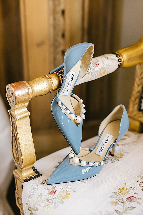 Bridal shoes in blue wedding heels with pearl strap, perched on a vintage floral chair with a gold wood frame detail