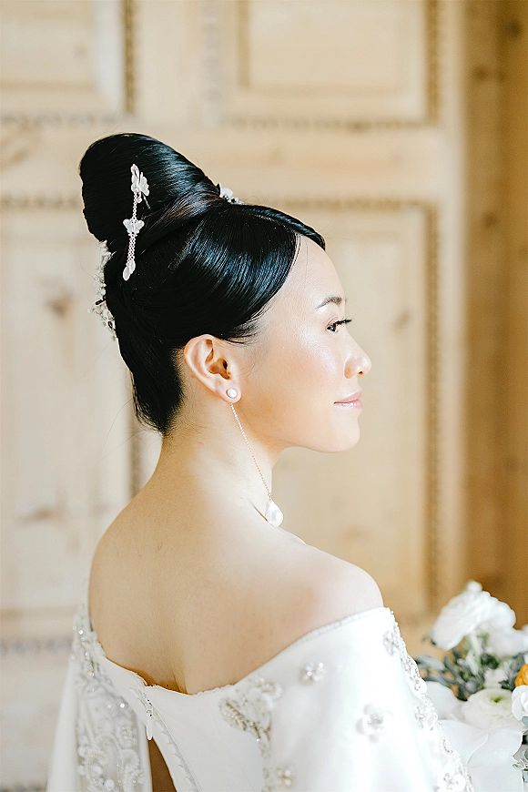 Bridal portrait of a bride in side profile with an elegant bridal updo, pearl hair pins, and off-shoulder beaded gown by neutral wall panels