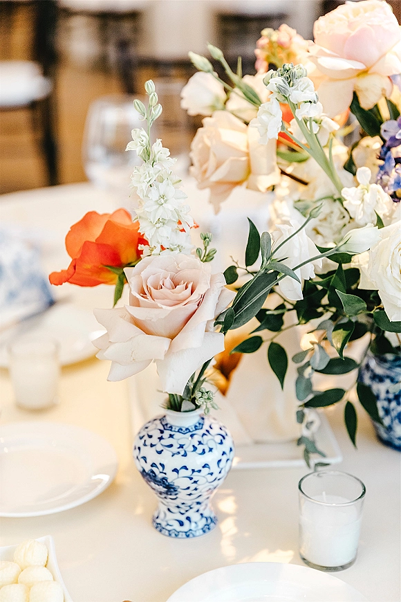 Wedding centerpiece with a blue and white vase centerpiece of roses and greenery, surrounded by taper and votive candles on a reception table