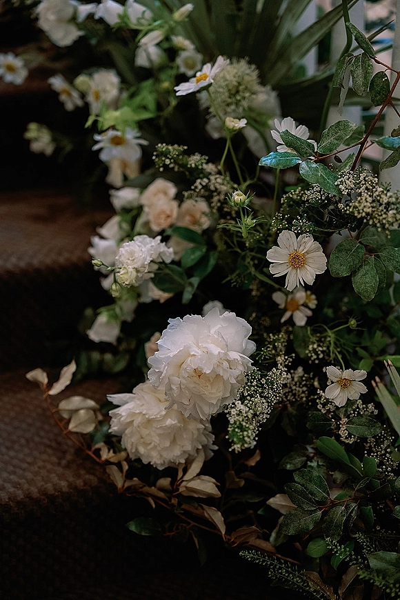 Wedding floral arrangement of white wedding flowers with peonies, daisies, eucalyptus, and baby’s breath tied to a white railing walkway