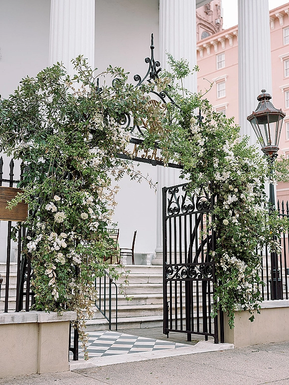 Wedding entrance florals with wrought iron gate flowers and white blooms, draped greenery garland framing steps on a checkered tile entryway