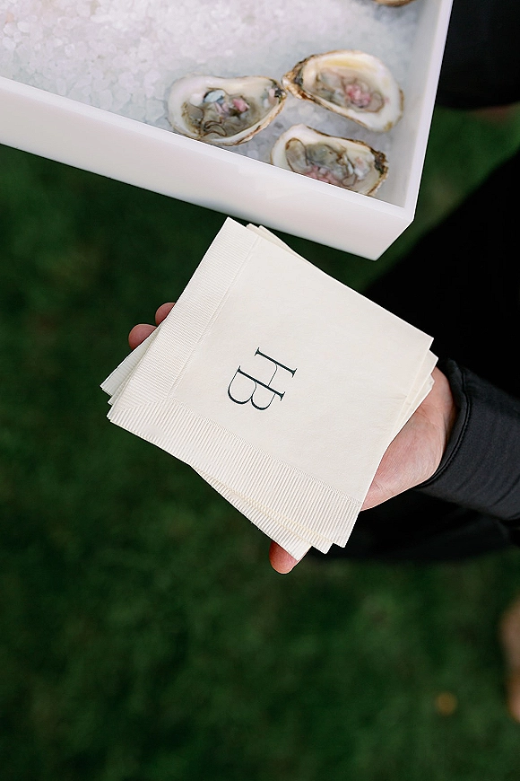 Wedding cocktail hour oyster bar wedding display with oysters on ice on a tray and monogrammed cocktail napkins on a grass lawn outdoors
