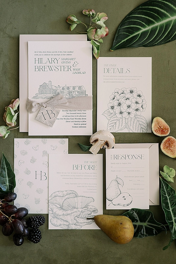 Invitation suite wedding invitation flat lay with envelopes, RSVP and monogram cards tied in ribbon on olive green surface with fruit accents