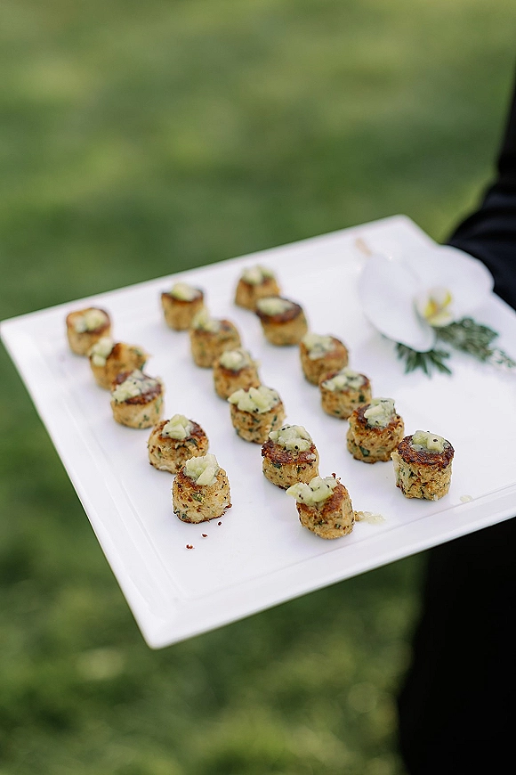 Wedding appetizers on a white serving tray with bite-size garnished canapes, passed hors doeuvres outdoors on a blurred green lawn