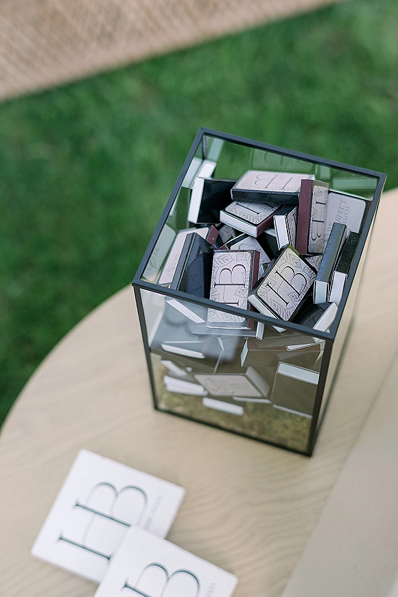 Wedding matchbooks arranged in a glass box, custom matchbooks wedding favor style, on a wood tabletop with grass lawn behind