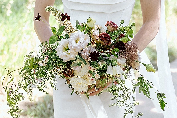 Bridal bouquet with garden style bridal bouquet roses, white lisianthus, wildflowers and trailing greenery against sunlit outdoor bokeh