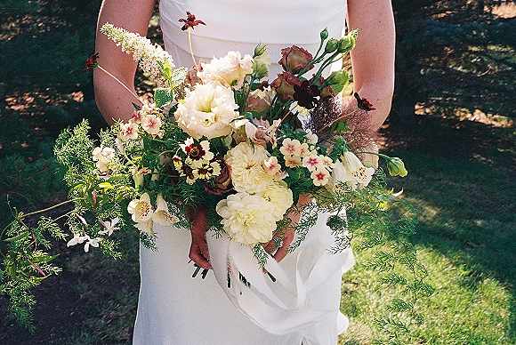 Bridal bouquet in a garden style wedding bouquet, mixed flowers and cascading greenery with long stems on a sunlit grass lawn