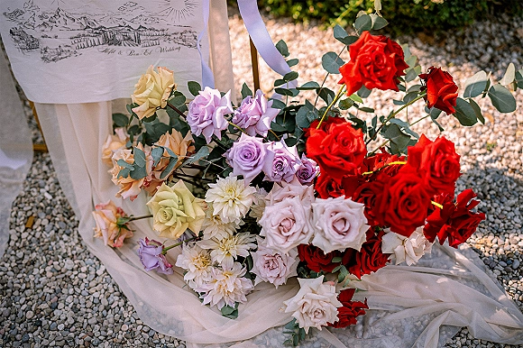 Wedding bouquet with a red rose wedding bouquet mix of blush and lavender roses, eucalyptus, and white ribbon on blush fabric by an illustrated sign