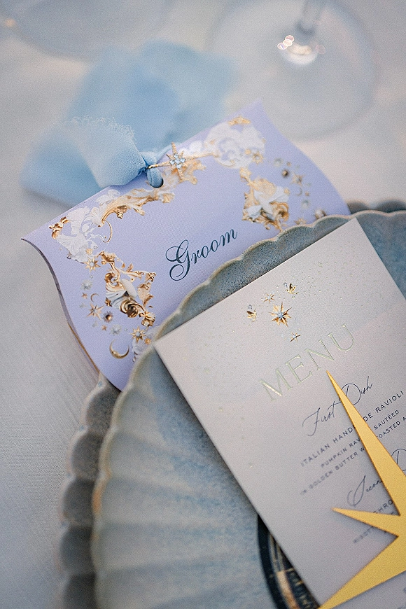 Wedding place setting with wedding menu card and gold foil details, silk ribbon place card on scalloped plate atop white tablecloth