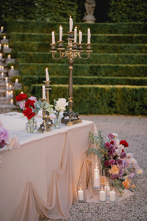 Wedding tablescape with candelabra wedding centerpiece, brass taper candles and roses with eucalyptus on neutral linen in a hedge garden setting