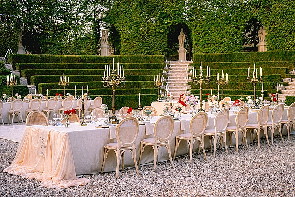 Reception tablescape for an outdoor wedding reception with long banquet tables, brass candelabras and florals in a formal hedge garden courtyard