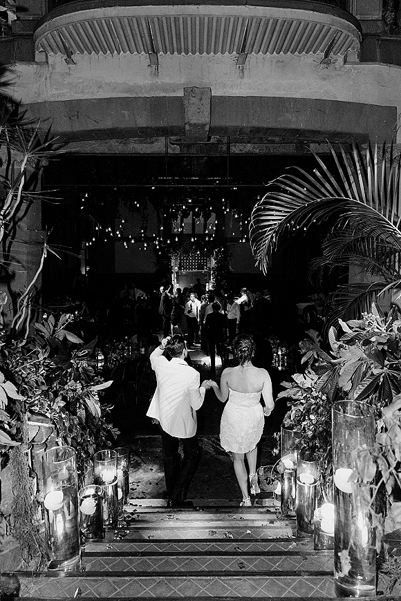 Wedding reception entrance with newlyweds entering reception down a stone staircase lined with glass cylinder candles and string lights among guests