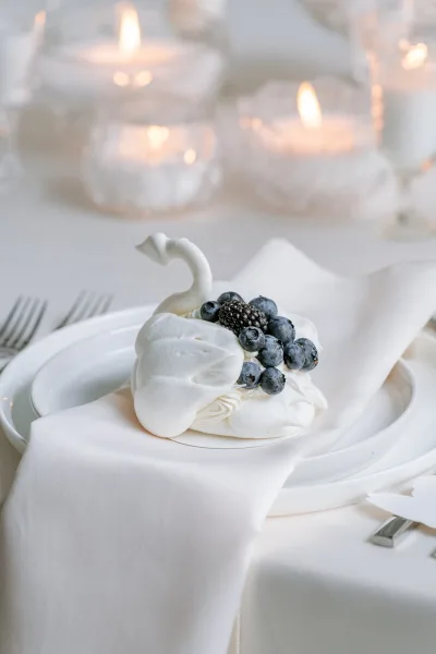 Wedding dessert: a mini pavlova dessert crowned with blueberries, glowing amid candles in glass votives on a white tablecloth.