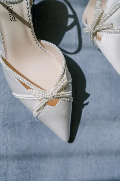 Bridal shoes with scalloped trim arranged toe-to-toe on softly textured blue fabric, highlighting delicate craftsmanship and poise.