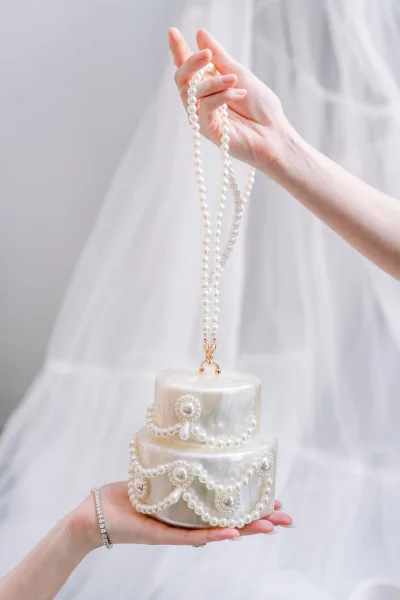 Bridal clutch, a pearl bridal bag, rests on a soft tulle veil against a clean white backdrop, styled simply.