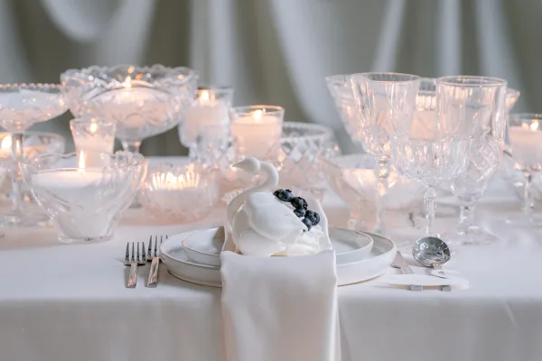 Wedding tablescape set for a candlelit reception table, crystal glassware gleaming against a soft draped fabric backdrop.