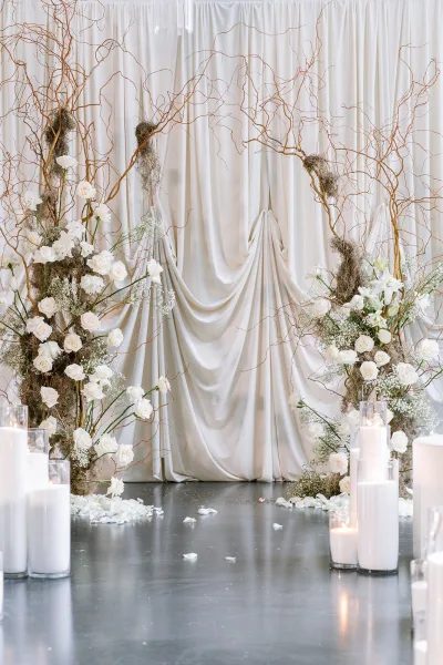 Ceremony backdrop featuring a draped fabric altar framed with white roses, set over a polished concrete floor.