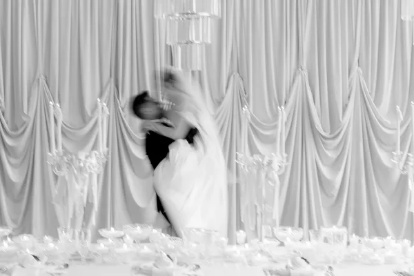Couple portrait of a bride and groom dip at the reception, her veil flowing as they lean by the reception table against soft drapery.